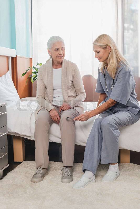 Nurse examining smiling senior woman with reflex hammer in hospital , stock photo