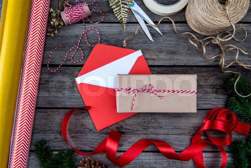 Top view of christmas gift, envelope with card, wrapping paper and red ribbon on wooden table top, stock photo