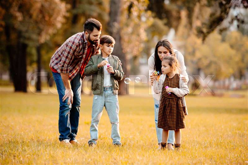 Young family with two children playing with soap bubbles in autumn park, stock photo