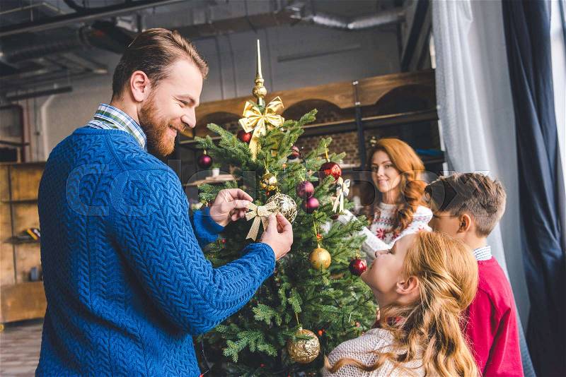 Young happy family decorating christmas tree at cozy modern apartments, stock photo