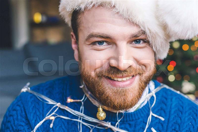 Close-up portrait of handsome bearded man tied up with christmas garland, stock photo