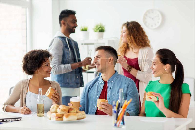 Corporate, celebration and people concept - happy friends or team eating sandwiches with coffee and non-alcoholic drinks at office party, stock photo