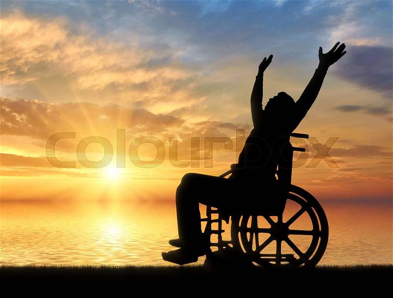 Happy disabled person in a wheelchair with arms raised on a background of sea sunset. The concept of happy people with disabilities, stock photo