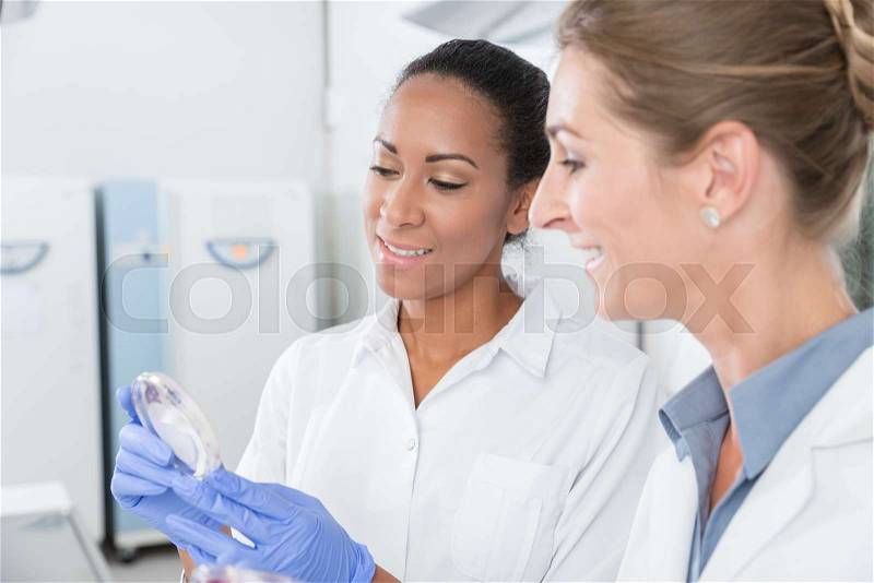 Scientists in research lab with analyzing instrument talking about test results, stock photo