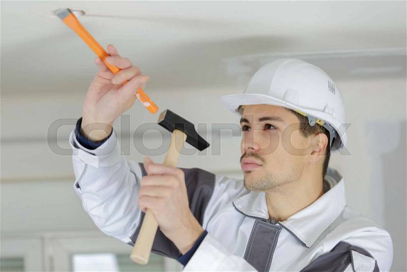 Young worker making hole in ceiling for light spot, stock photo