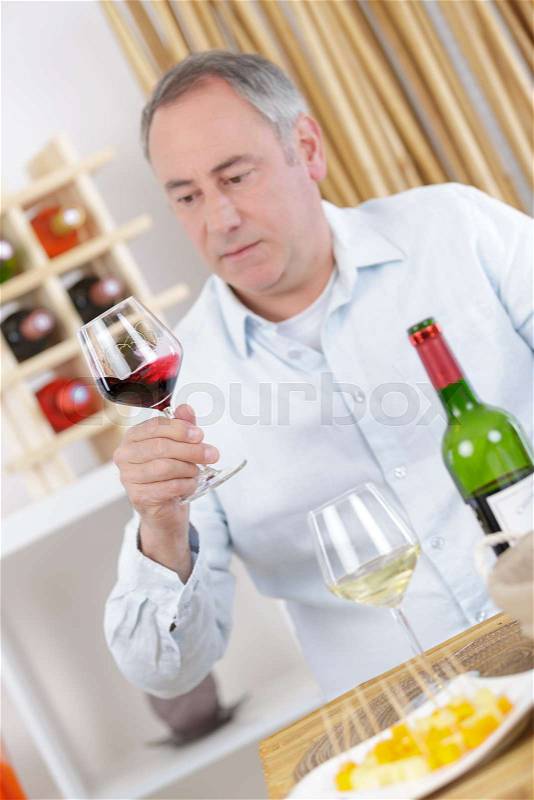 Mature man drinking a glass of red wine at home, stock photo