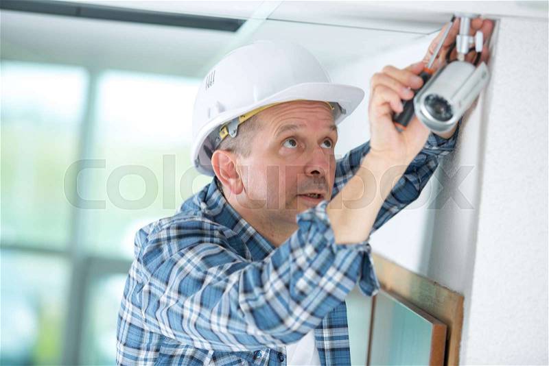 Technician worker installing video surveillance camera on wall, stock photo