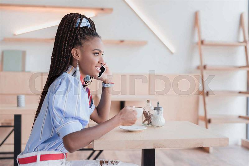 Young african american woman talking on phone in a coffee shop, stock photo