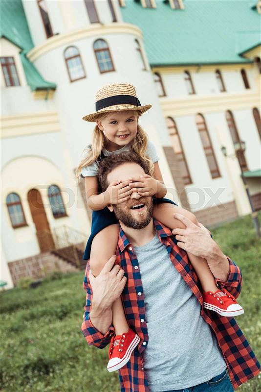 Little girl covering fathers eyes while piggybacking together, stock photo