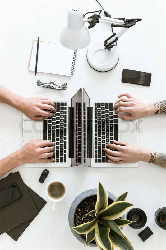 Top view of workspace with two laptops placed back to back while two men are working with them, stock photo