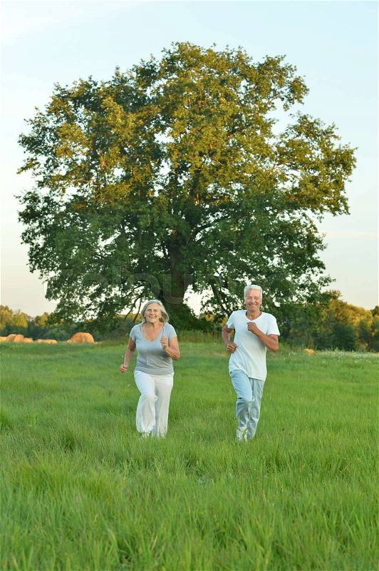 Portrait of beautiful caucasian senior couple running in field, stock photo