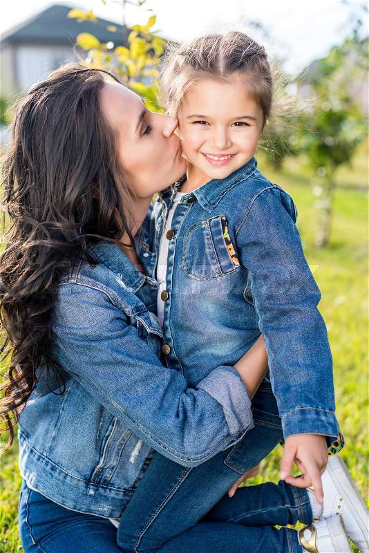 Mother kissing beautiful smiling daughter outdoors, stock photo