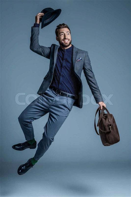 Smiling young man in suit jumping up and raising his hat, stock photo
