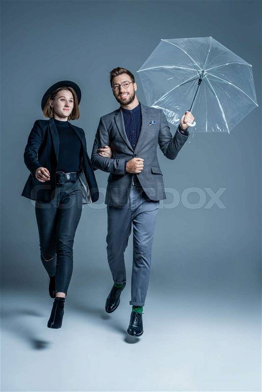 Man in suit walking arm in arm with young woman and holding an umbrella, stock photo