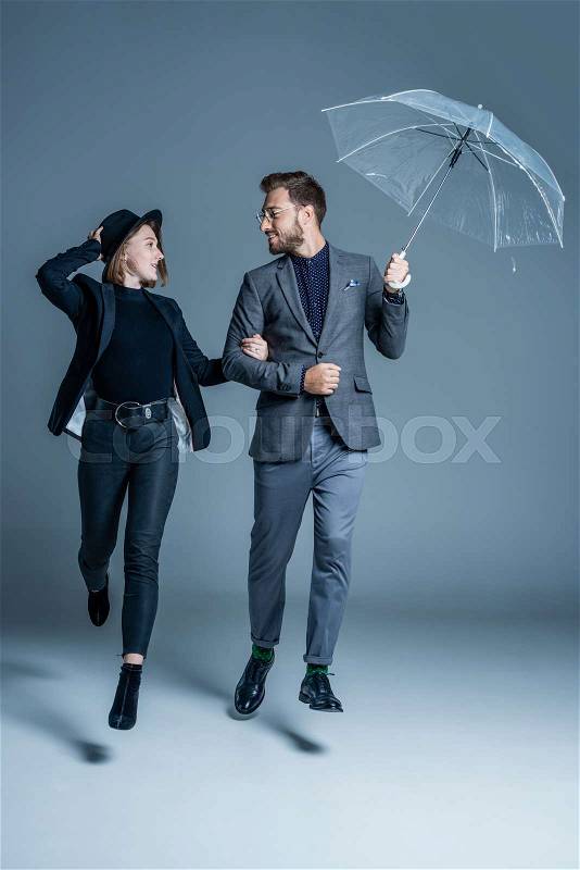 Man in suit walking arm in arm with young woman and holding an umbrella, stock photo