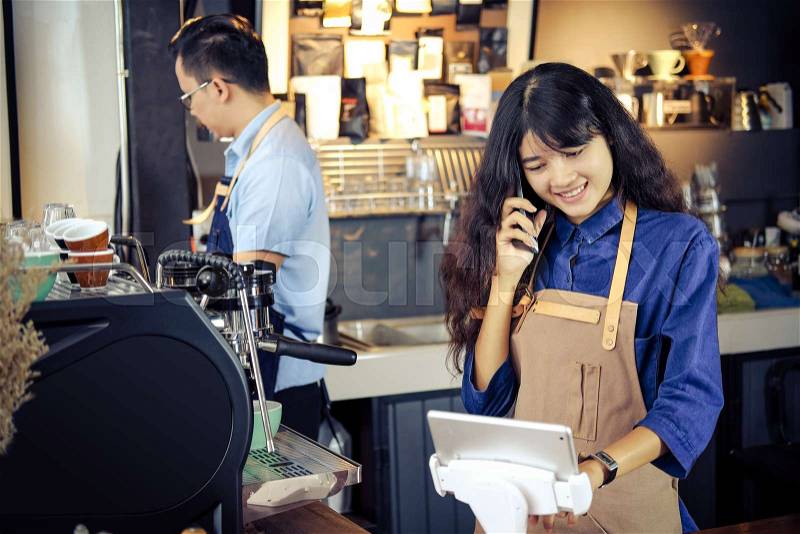 Asian barista talking order by phone in her shop. Cafe restaurant service, Small business owner, food and drink industry concept, stock photo