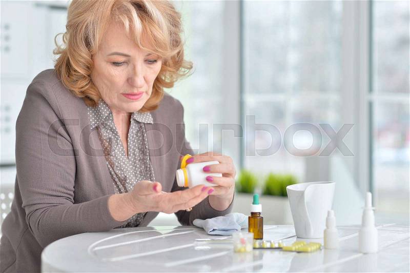 Sick senior woman taking medicines at home, stock photo