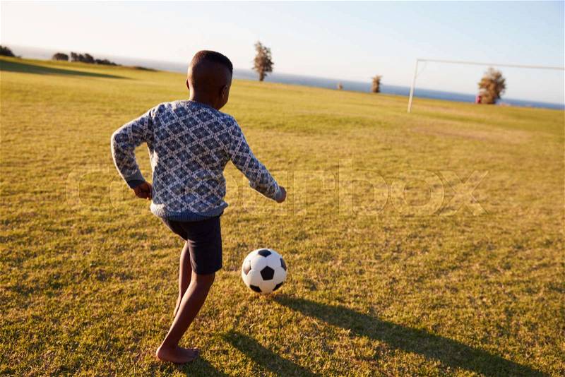 Elementary school boy playing football in an open field, stock photo