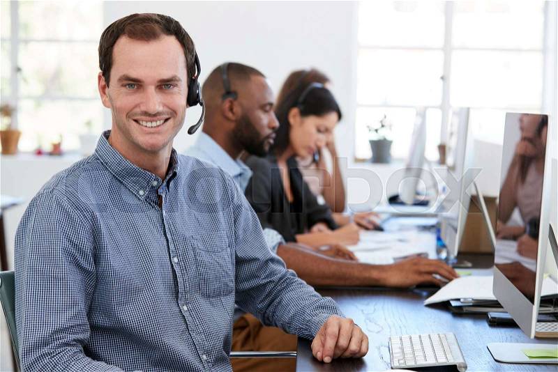 Young white man with headset on smiling to camera in office, stock photo