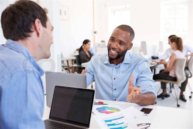 Two men discussing business in a busy office, stock photo