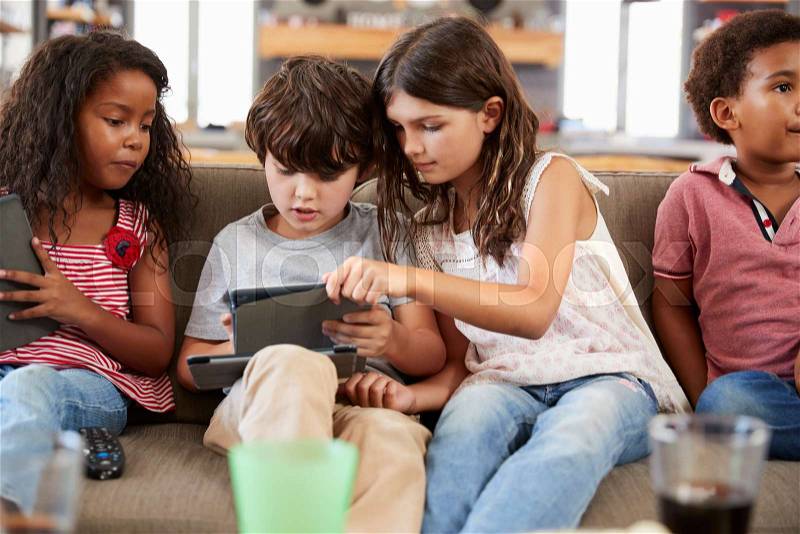 Group Of Children Sitting On Sofa Using Digital Devices, stock photo