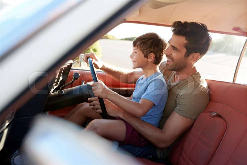 Father Teaching Young Son To Drive Car On Road Trip, stock photo