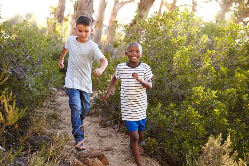 Two smiling young boys racing on a forest path, stock photo