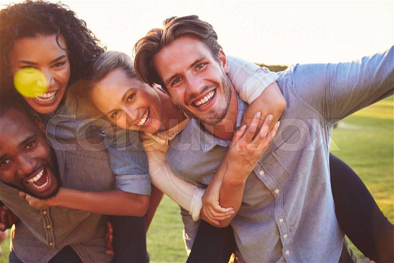Two laughing couples piggybacking outdoors, close up, stock photo
