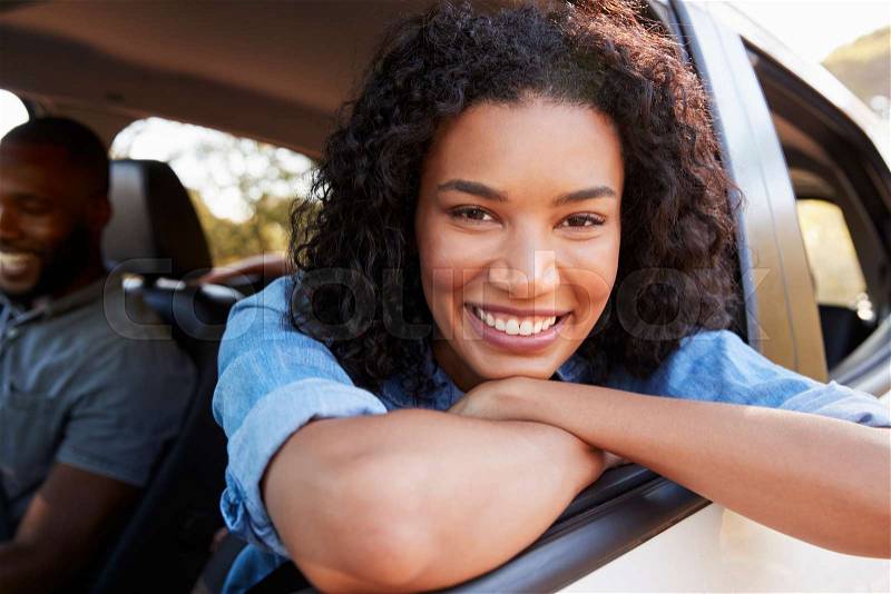 Young black woman looking out of car window smiles to camera, stock photo