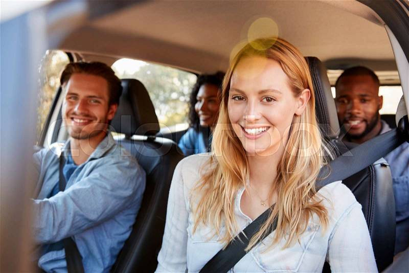 Four adult friends in a car on a road trip smiling to camera, stock photo