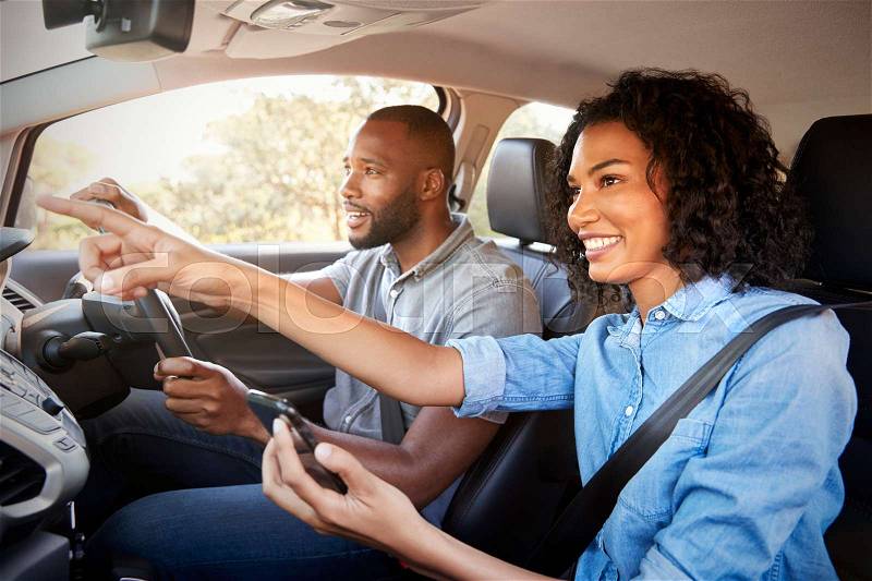 Happy couple in car on a road trip navigate with smartphone, stock photo