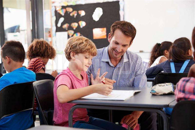 Teacher and young school boy looking at notebook in class, stock photo