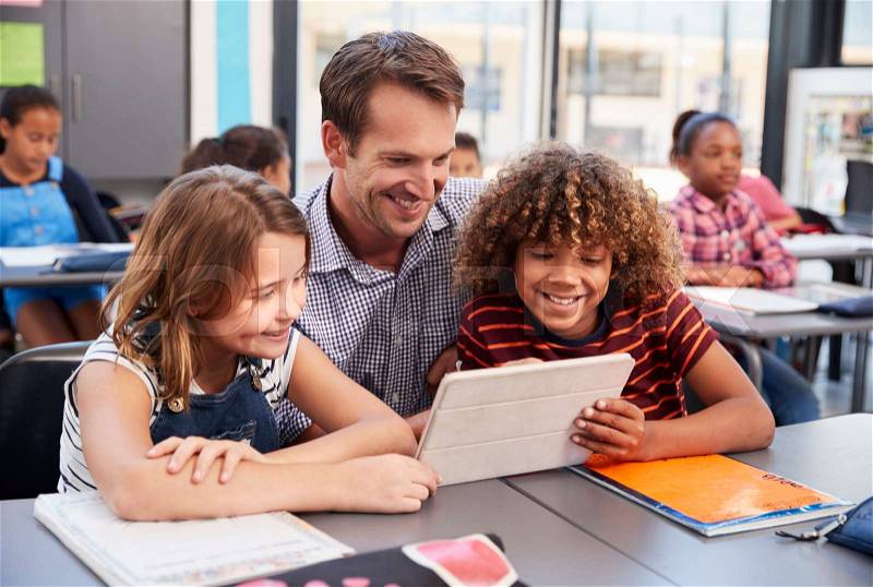 Teacher using tablet with two pupils in school class, stock photo
