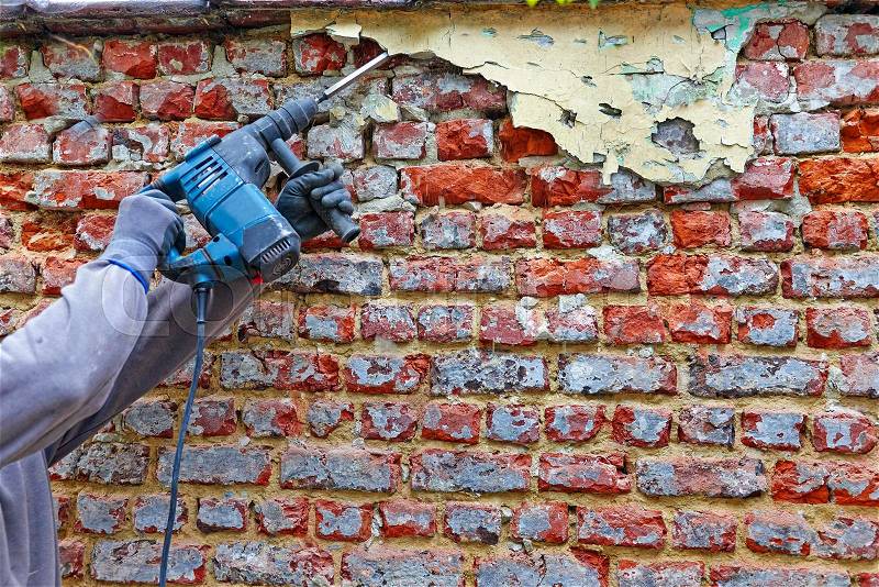 Worker with electrical hammer cleaning red brick wall outdoor, stock photo