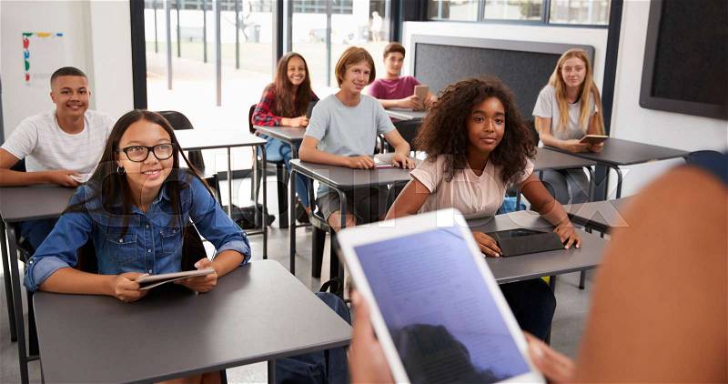 Teacher uses tablet in high school class, over shoulder view, stock photo