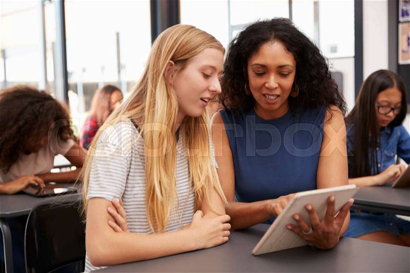 Teacher helps blonde teenage schoolgirl with tablet computer, stock photo