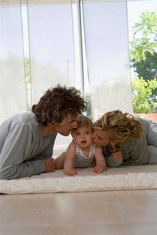 Parents kiss baby\'s cheeks, living floor, stock photo