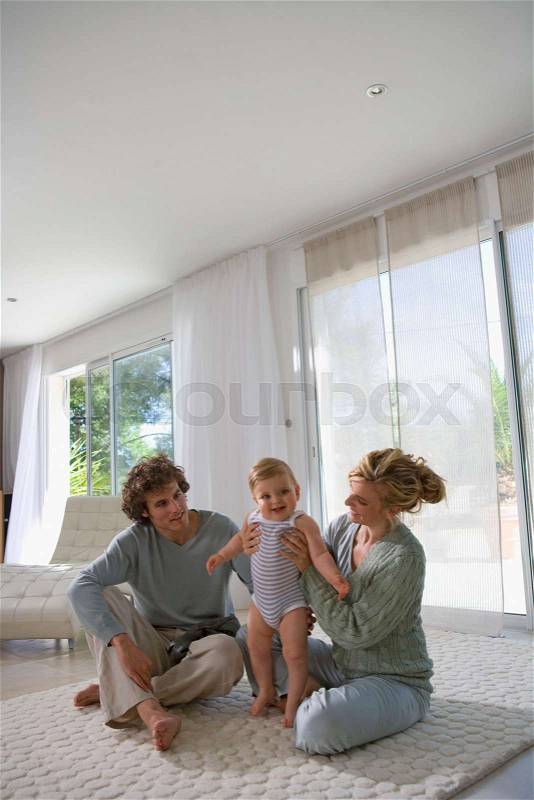Parents help baby stand up, home, stock photo
