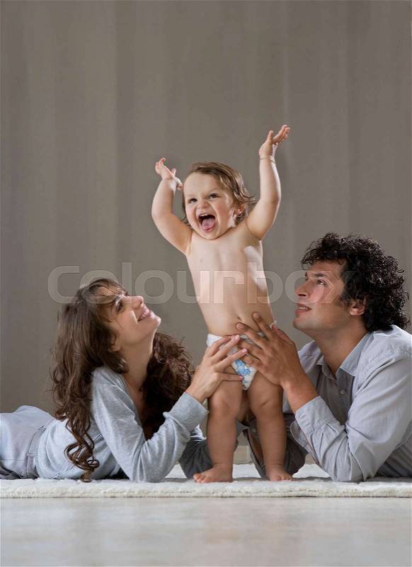 Parents helping baby to stand up, stock photo