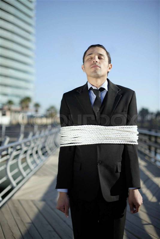 Business man tied up with ropes outdoors, stock photo