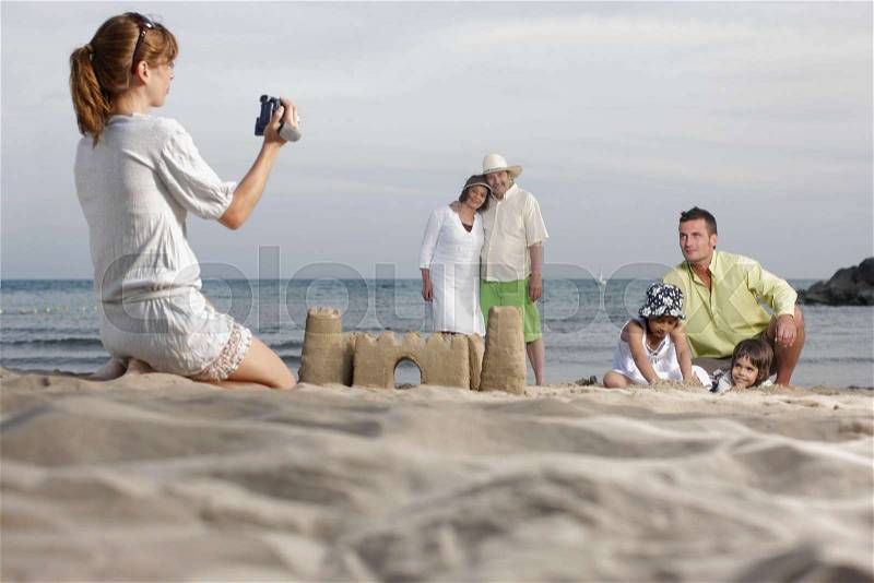 Mother taking video of family on beach, stock photo