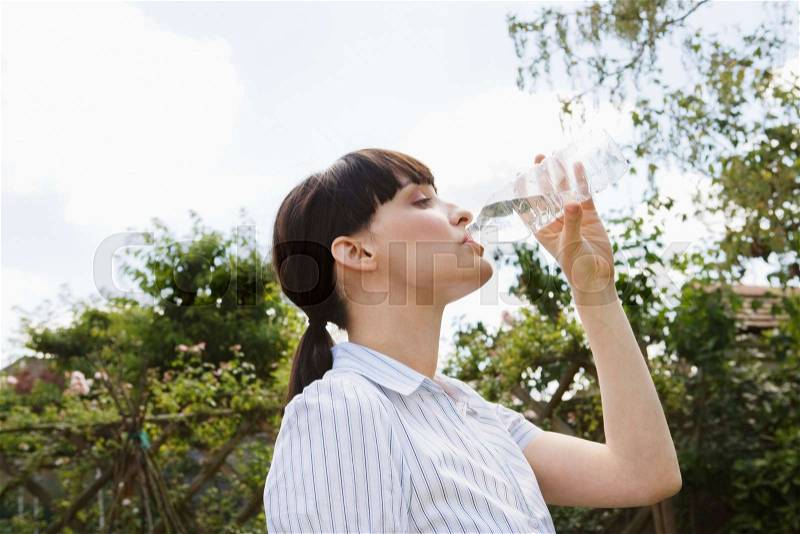 Woman drinking from water bottle in park, stock photo