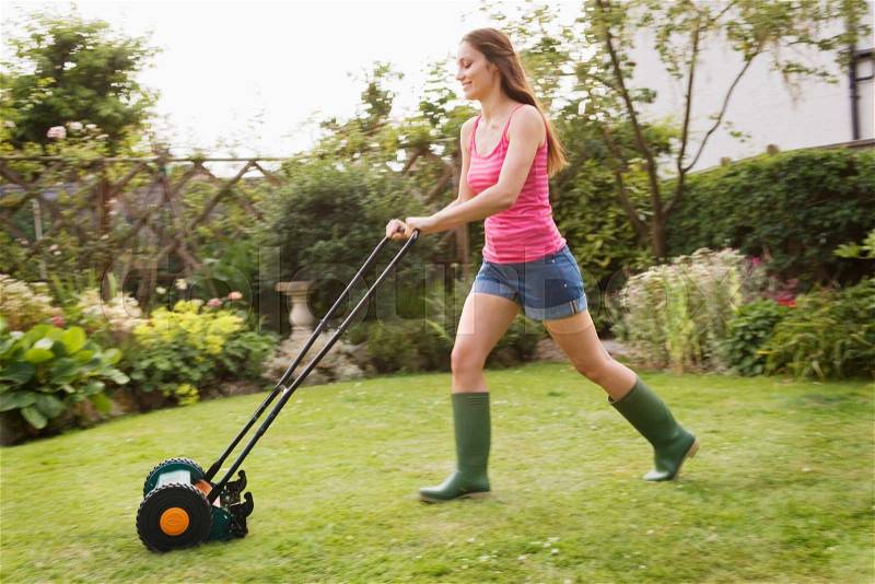 Woman mowing lawn with grass mower, stock photo