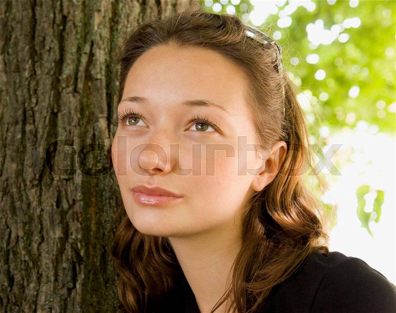 Girl leaning against a tree looking up, stock photo