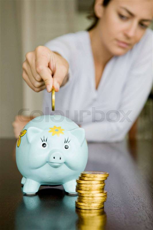 Woman dropping money into a piggy bank, stock photo