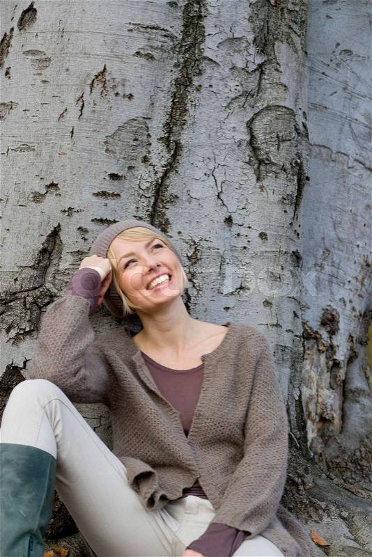 Woman leaning at tree laughing, stock photo