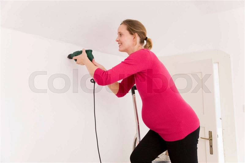 Pregnant woman with power drill, stock photo