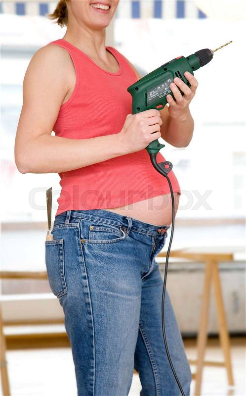 Pregnant woman with power drill, stock photo