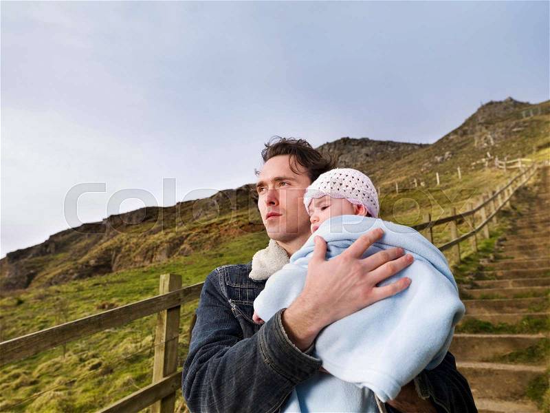 Man on hill path holding baby, stock photo