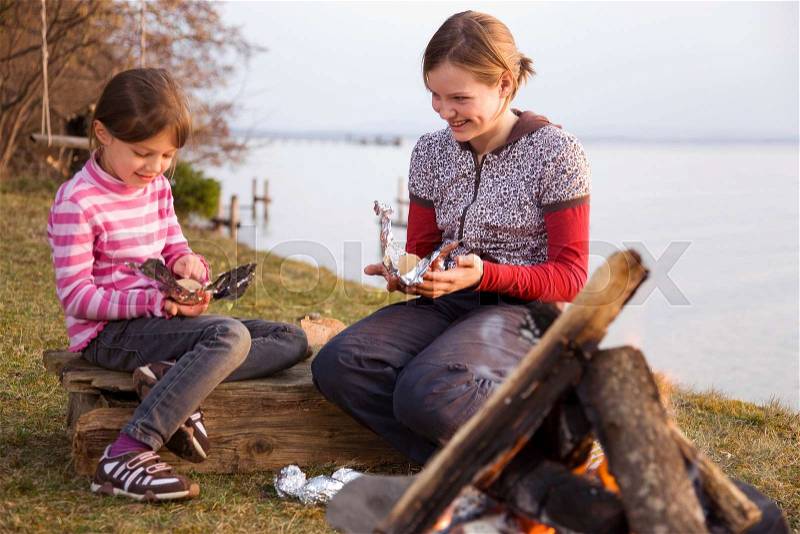 Two girls wrapping potatoes for barbecue, stock photo